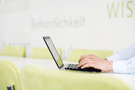 Eine Person am Laptop in einer Corporate Architektur Umgebung. Die Businessfotografie zeigt das entspannte Arbeiten in einer Bonner Firma.